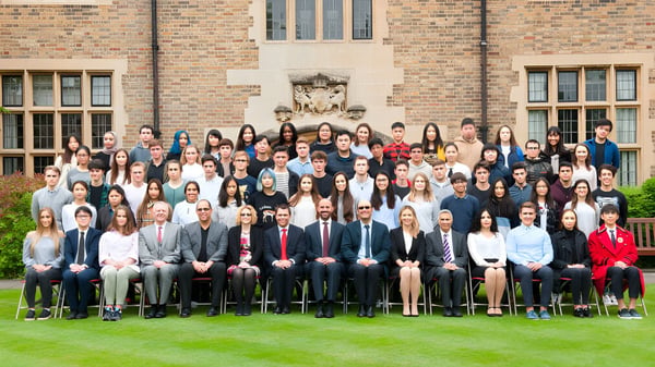 Eine Gruppe von Schülern steht und sitzt vor einem Backsteingebäude auf dem Campus von MPW Cambridge.