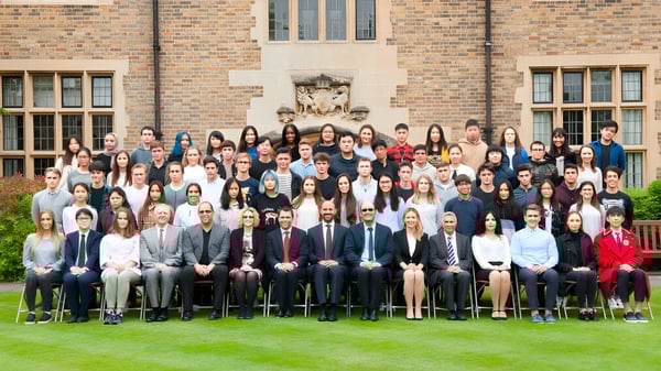 Eine Gruppe von Schülern steht und sitzt vor einem Backsteingebäude auf dem Campus von MPW Cambridge.
