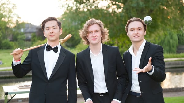 Drei junge Männer stehen in einem parkähnlichen Bereich auf dem Campus der MPW Cambridge Schule.