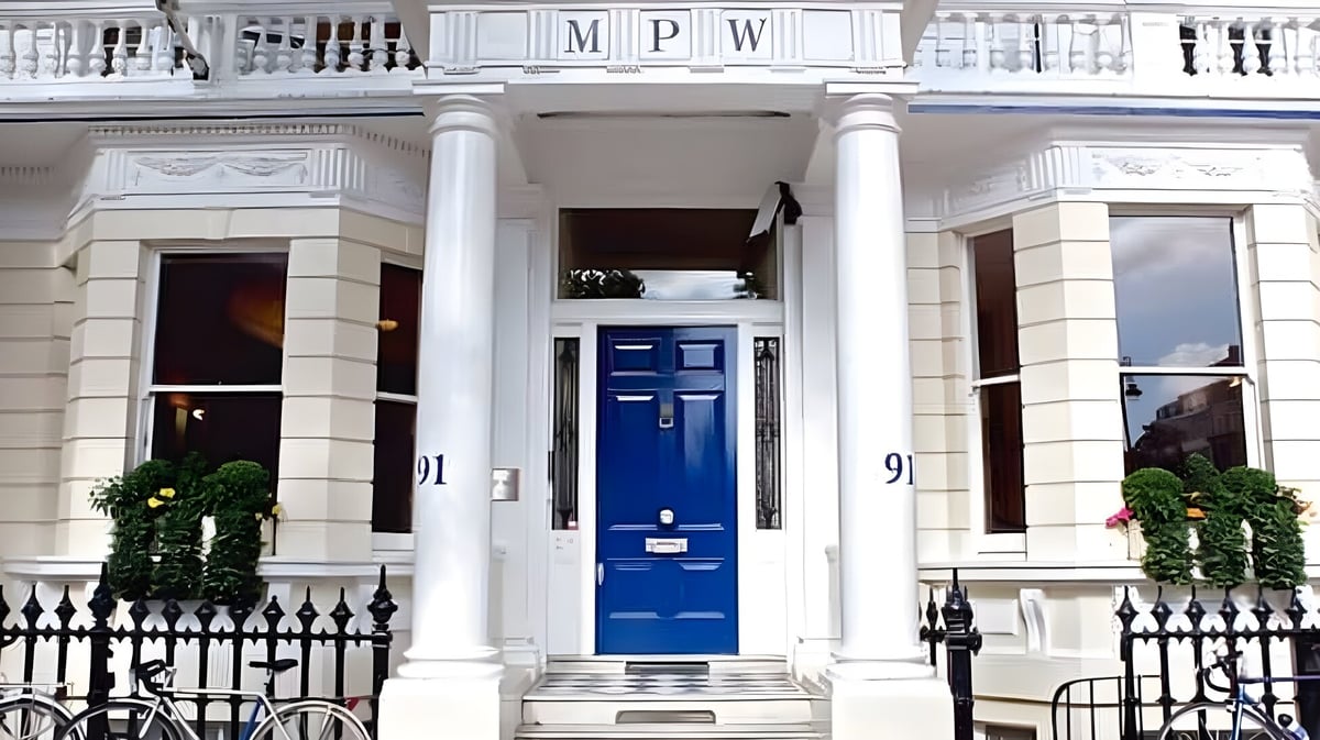Das Gebäude der MPW London zeigt weiße Säulen und eine blaue Eingangstür mit einem schmiedeeisernen Zaun im Vordergrund.