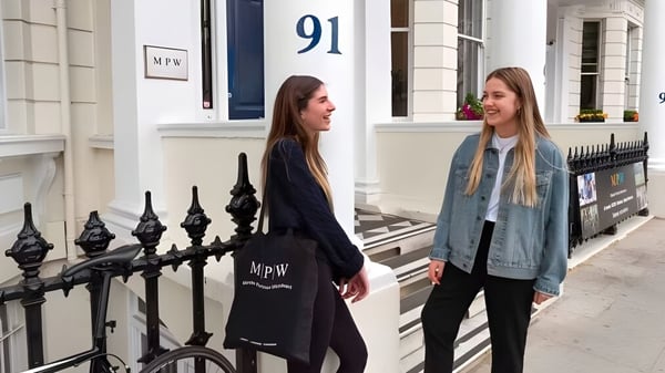 Zwei Schülerinnen stehen vor einem Gebäude mit der Nummer 91 auf dem Campus der MPW London und unterhalten sich.