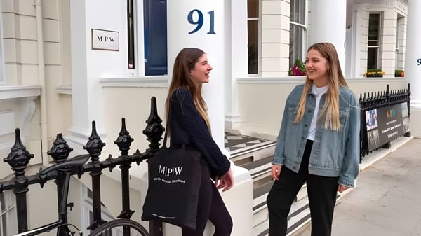 Zwei Schuelerinnen stehen vor einem Gebaeude auf dem Campus der MPW London und unterhalten sich.