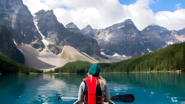 Eine Person in roter Jacke steht an einem türkisfarbenen Bergsee mit schneebedeckten Bergen im Hintergrund auf dem Gelände der Mt. Sentinel Secondary School.