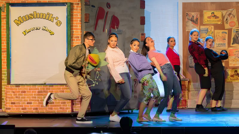 Eine Gruppe von Schülerinnen und Schülern steht in bunten Outfits auf der Bühne im Mullingar Community College vor einer Backsteinwand mit dem Schriftzug Musique.