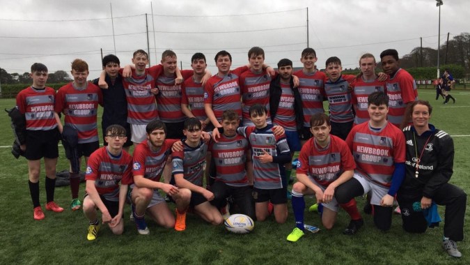 Eine Gruppe von Schülerinnen und Schülern des Mullingar Community College posiert gemeinsam auf einem Fußballfeld unter bewölktem Himmel.