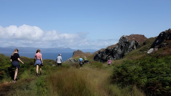 Schüler des Mullingar Community College wandern auf einem Pfad durch eine grüne Landschaft mit Bergen und Wasser im Hintergrund.