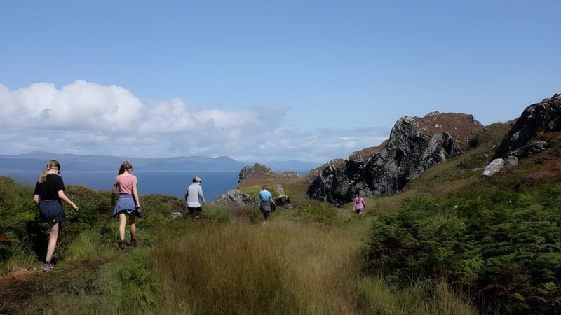 Schüler des Mullingar Community College wandern auf einem Pfad durch eine grüne Landschaft mit Bergen und Wasser im Hintergrund.