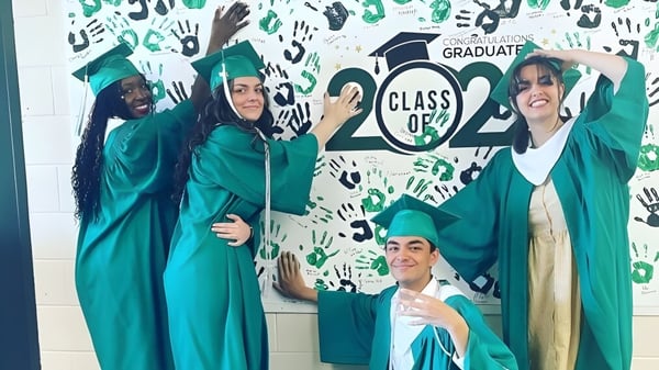 Absolventinnen und Absolventen des Murdoch Mackay Collegiate in grünen Talaren posieren vor einem Hintergrund mit der Aufschrift CLASS OF 2024 und Handabdrücken.