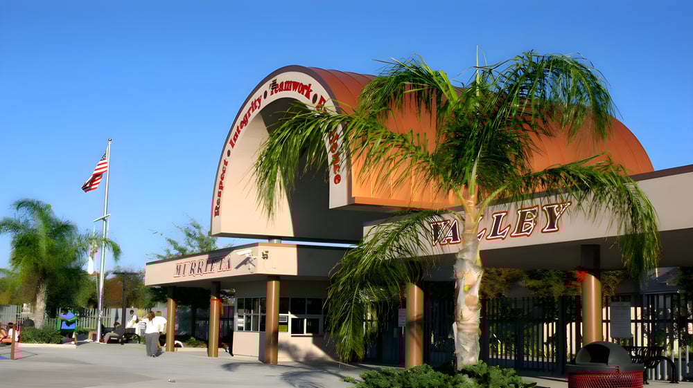 Das orangefarbene Gebäude mit dem markanten Bogen am Eingang gehört zur Murietta Valley High School und ist von Palmen umgeben.