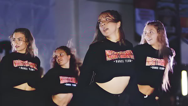 Eine Gruppe Schülerinnen der Murietta Valley High School trägt schwarze Kapuzenpullover mit einem besonderen Logo in einem schwach beleuchteten Raum.