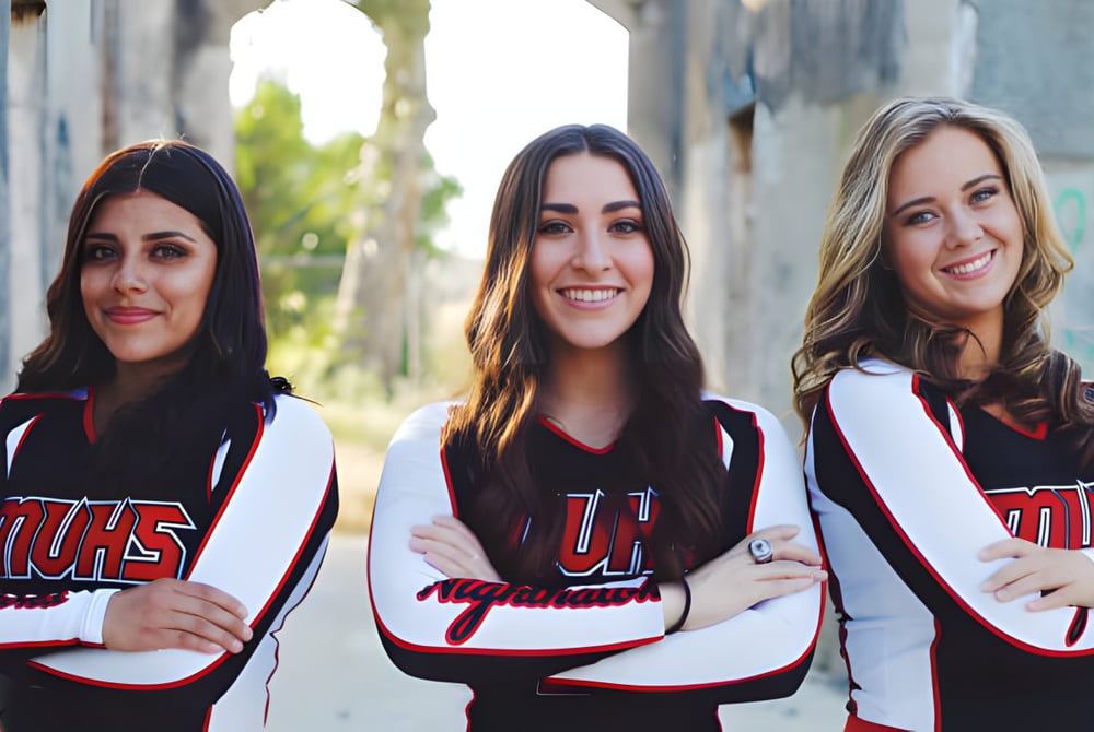 Drei Schülerinnen der Murietta Valley High School stehen vor einer Backsteinmauer und tragen gleiche Sporttrikots mit dem Schriftzug UHS.