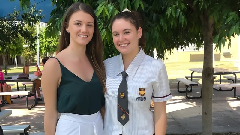 Zwei Schülerinnen stehen im Freien auf dem Campus des Murrumba State Secondary College vor Bäumen und einem Gebäude.