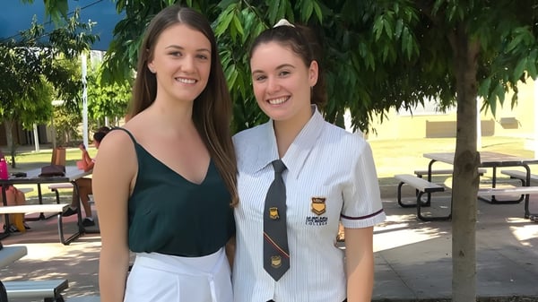 Zwei Schülerinnen stehen im Freien auf dem Campus des Murrumba State Secondary College vor Bäumen und einem Gebäude.