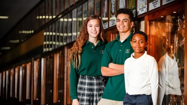Drei Schülerinnen und Schüler der Muskegon Catholic Central High School stehen gemeinsam im Schulflur vor Schließfächern.