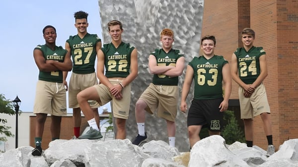 Eine Gruppe von Sportlern steht auf einem felsigen Vorsprung vor einem Gebäude auf dem Campus der Muskegon Catholic Central High School.
