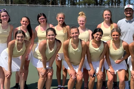 Eine Gruppe von Schülerinnen der Muskegon Catholic Central High School posiert auf dem Tennisplatz vor einem bewaldeten Hintergrund.
