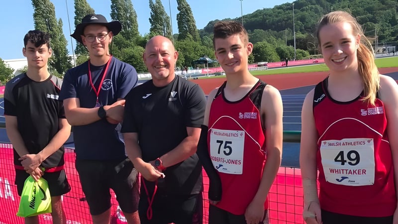 Eine Gruppe von Athleten steht auf der Laufbahn des Myddelton College vor Bäumen und Gebäuden.