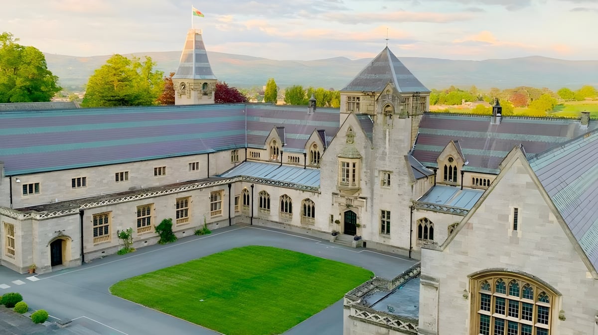 Das mittelalterlich anmutende Schloss des Myddelton College mit Türmen und einem grünen Innenhof vor Bergkulisse.
