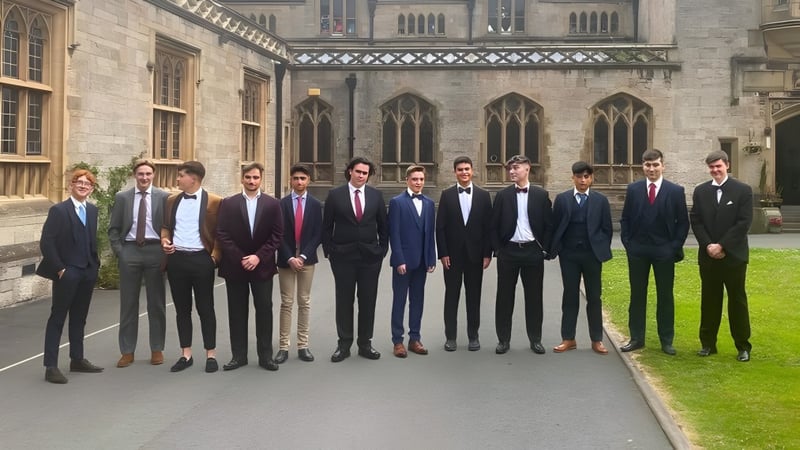 Eine Gruppe von Männern in formeller Kleidung steht vor dem gotischen Hauptgebäude von Myddelton College.