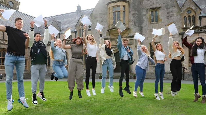 Eine Gruppe Schülerinnen und Schüler des Myddelton College steht auf einer Wiese vor einem historischen Gebäude und winkt mit weißen Fahnen.