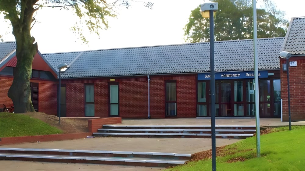 Das Backsteingebäude mit schrägem Dach und großen Fenstern auf dem Campus des Nagle Community College ist von Bäumen und einer Grasfläche umgeben.