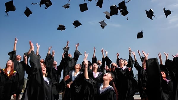 Absolventinnen und Absolventen der Nakusp Secondary School werfen ihre Abschlussmützen in den klaren Himmel.