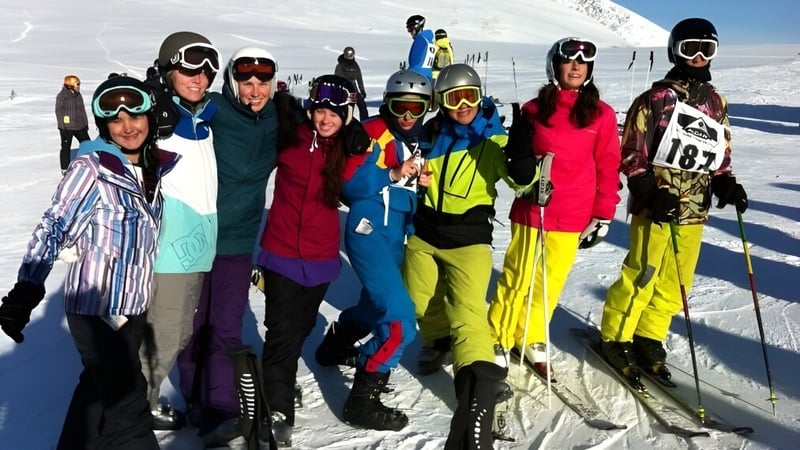 Schüler der Nakusp Secondary School in bunter Skiausrüstung stehen auf einer schneebedeckten Piste vor Bergen.