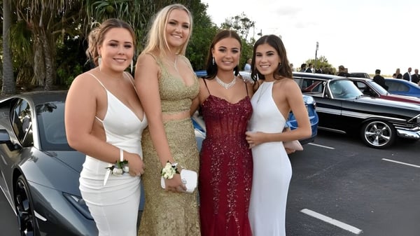 Vier Schülerinnen des Nambour State College posieren vor einem Luxusfahrzeug in einer Außenanlage mit Palmen.