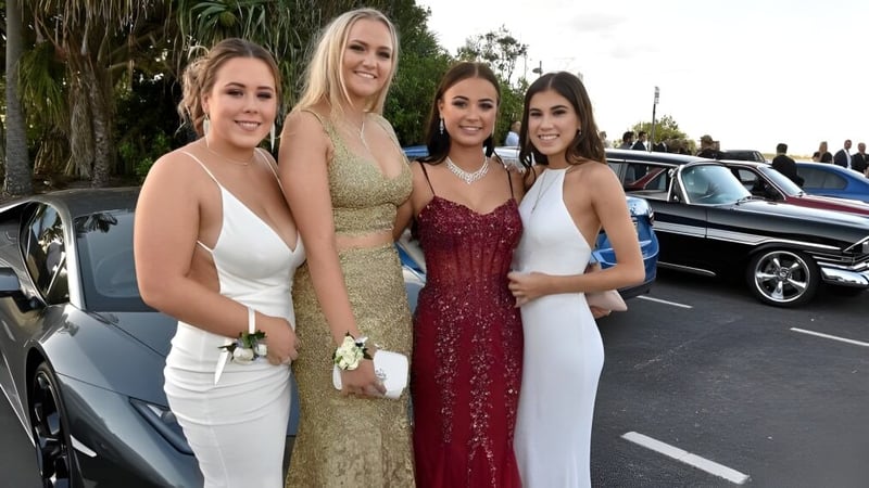 Vier Schülerinnen des Nambour State College posieren vor einem Luxusfahrzeug in einer Außenanlage mit Palmen.