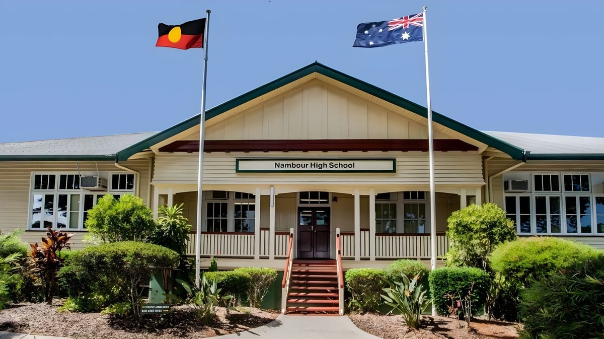Das hölzerne Schulgebäude von Nambour State College mit Veranda und Treppen sowie den Flaggen von Australien und den Aborigines.