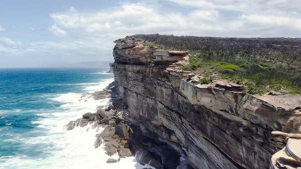 Ein felsiger Klippenabschnitt mit üppiger Vegetation blickt auf das türkisfarbene Meer am Nambour State College.
