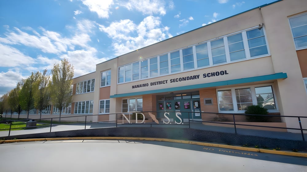 Das moderne mehrstöckige Schulgebäude der Nanaimo District Secondary School mit großen Fenstern unter blauem Himmel.