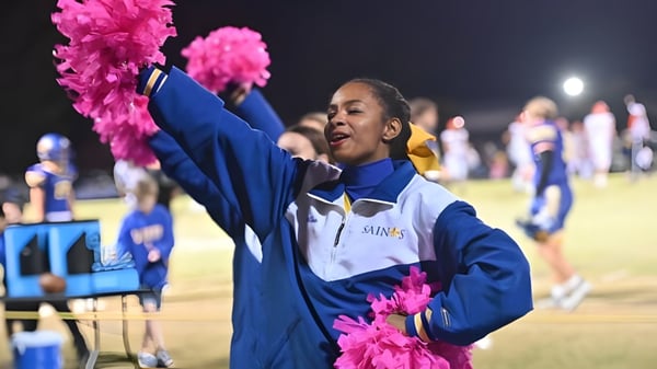 Eine Schülerin der Nansemond-Suffolk Academy hält pinke Pompons und führt auf dem Sportfeld bei Nacht eine Cheerleading-Performance durch.
