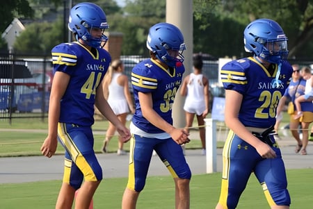 Drei Fußballspieler der Nansemond-Suffolk Academy stehen auf dem Rasen vor einem Schulgebäude.