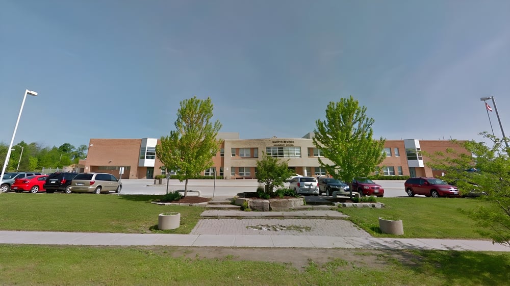 Das mehrstöckige Backsteingebäude der Nantyr Shores Secondary School mit einer Grünfläche und Bäumen im Vordergrund ist von einem gepflasterten Parkplatz umgeben.