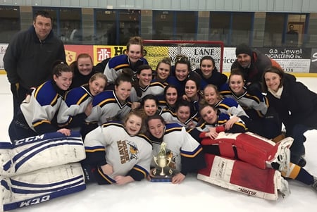 Schülerinnen der Napanee District Secondary School feiern mit einer Trophäe ihren Sieg auf dem Eis.