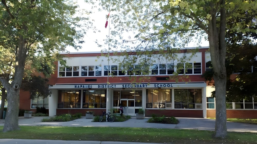 Das zweistöckige Backsteingebäude der Napanee District Secondary School steht auf einer Wiese umgeben von Bäumen.
