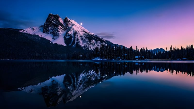 Ein ruhiger Bergsee spiegelt die schneebedeckten Gipfel und den Abendhimmel in der Landschaft nahe der Napanee District Secondary School.