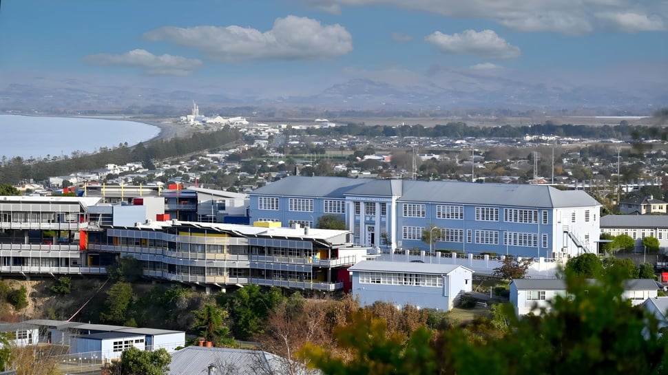 Blick von der Napier Girls' High School auf eine Stadtlandschaft mit bunten Gebäuden und Bergen im Hintergrund unter bewölktem Himmel.