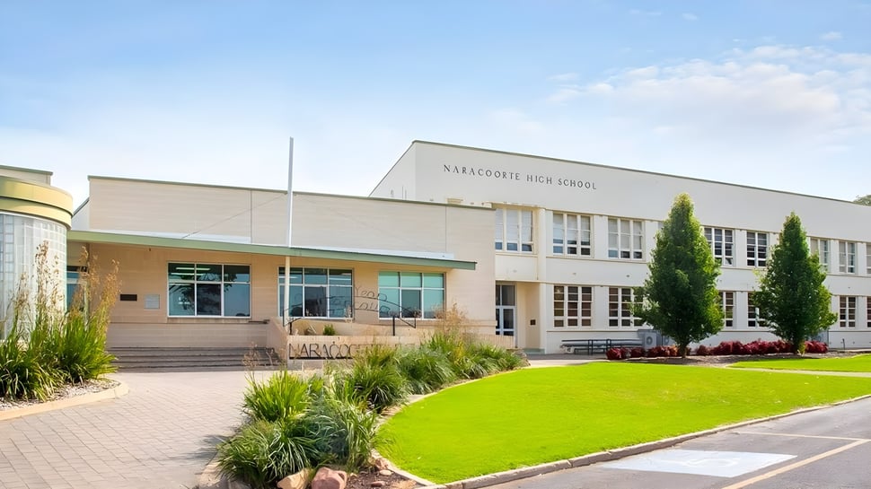 Das moderne mehrstöckige Schulgebäude der Naracoorte High School mit gepflegtem Rasen und Bepflanzung im Vordergrund unter blauem Himmel.