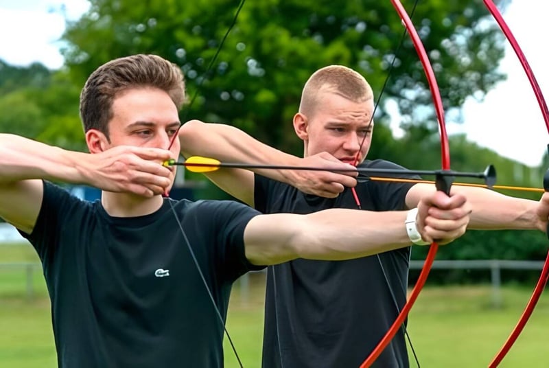 Zwei Männer zielen mit Pfeil und Bogen auf ein Ziel im Freien auf dem Campus des National Mathematics & Science College.