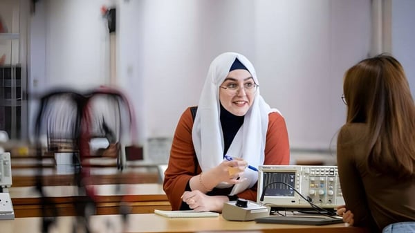 Eine Frau mit Hijab steht an einem Empfangsschalter und spricht mit einer Person auf dem Campus des National Mathematics and Science College.