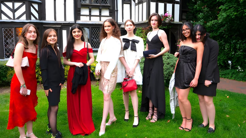 Eine Gruppe modisch gekleideter Frauen steht vor einem historischen Tudor-Gebäude auf dem Campus des National Mathematics & Science College.