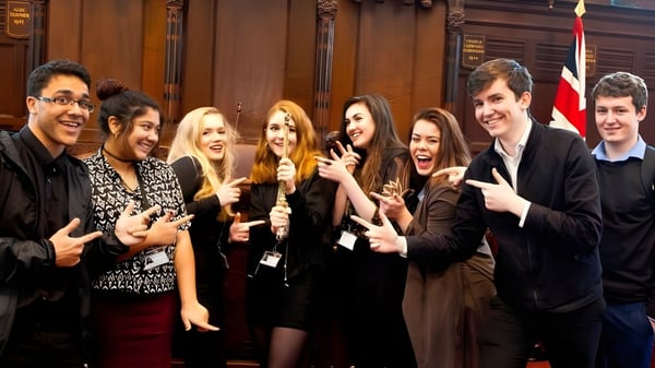 Eine Gruppe Schülerinnen und Schüler steht im National Mathematics & Science College vor einem mit Holzvertäfelung verzierten Hintergrund.