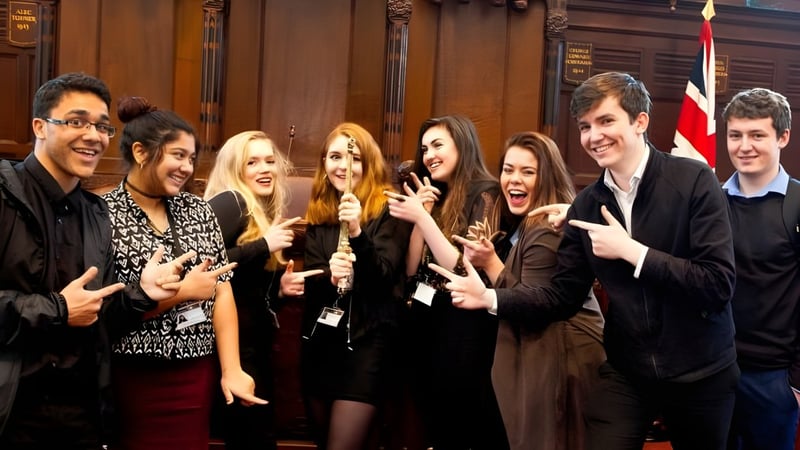Eine Gruppe Schülerinnen und Schüler steht im National Mathematics & Science College vor einem mit Holzvertäfelung verzierten Hintergrund.