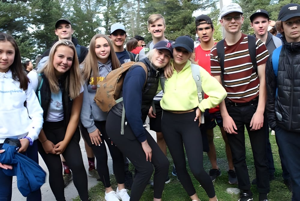 Eine Gruppe von Schülerinnen und Schülern steht gemeinsam draußen in einer parkähnlichen Umgebung auf dem Gelände der National Sport School.