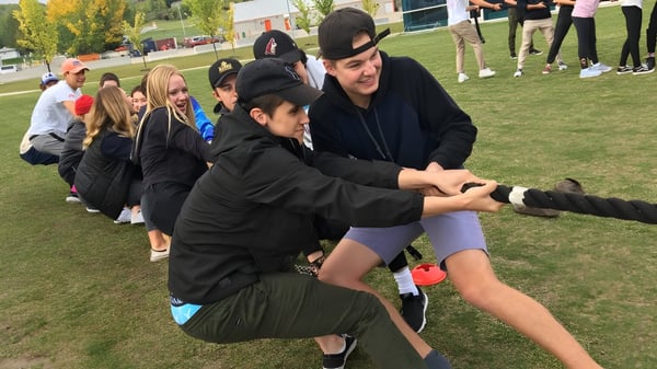 Eine Gruppe von Schülerinnen und Schülern der National Sport School spielt ein Spiel auf einem Sportfeld mit Gebäuden und Bäumen im Hintergrund.