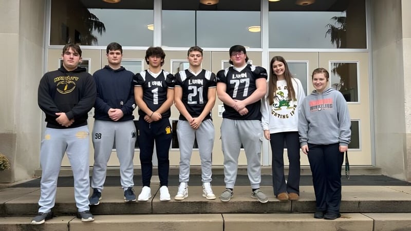 Eine Sportmannschaft auf den Treppen vor dem Gebäude der Nativity BVM High School mit Palmen im Hintergrund.