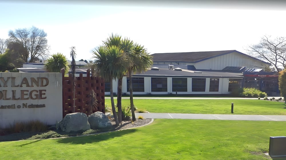 Der Eingang von Nayland College mit einem Schild und einer Grünfläche mit Palmen im Vordergrund.