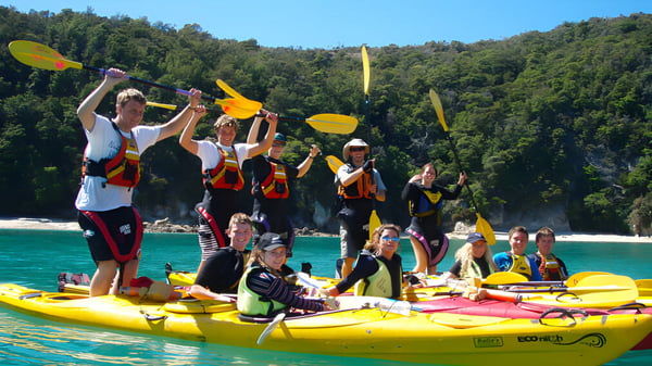 Schüler des Nayland College paddeln mit bunten Schwimmwesten und Helmen auf gelben Kajaks auf einem türkisfarbenen Gewässer.